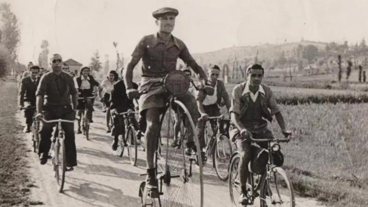 Fotografia d'epoca con un uomo su un biciclo seguito da altre persone in bicicletta