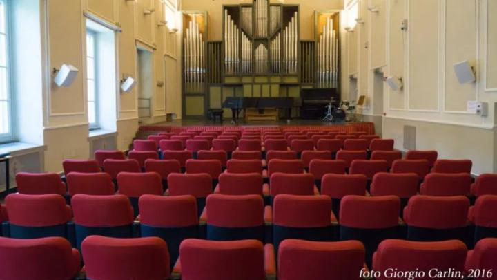 Interno di sala da concerto con sullo sfondo palco con grande organo a canne