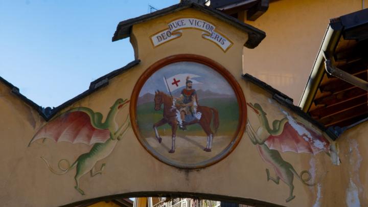 Particolare di un arco in muratura nel centro storico di Borgo San Dalmazzo: in alto, un tondo dipinto con un santo vestito da soldato romano,  a cavallo, ai lati due draghi. 