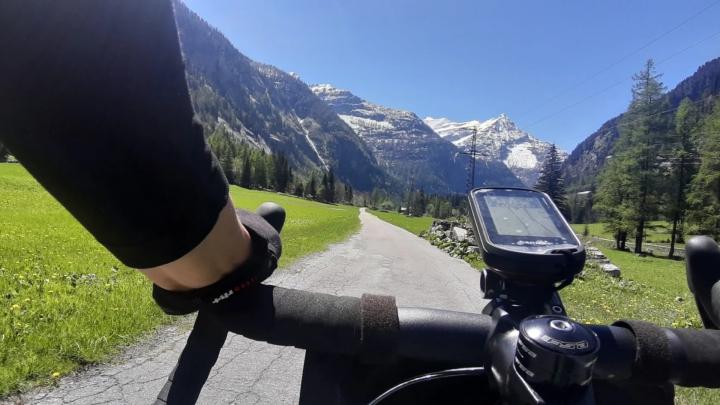 Strada in valle di montagna con in primo piano manubrio di mountain bike