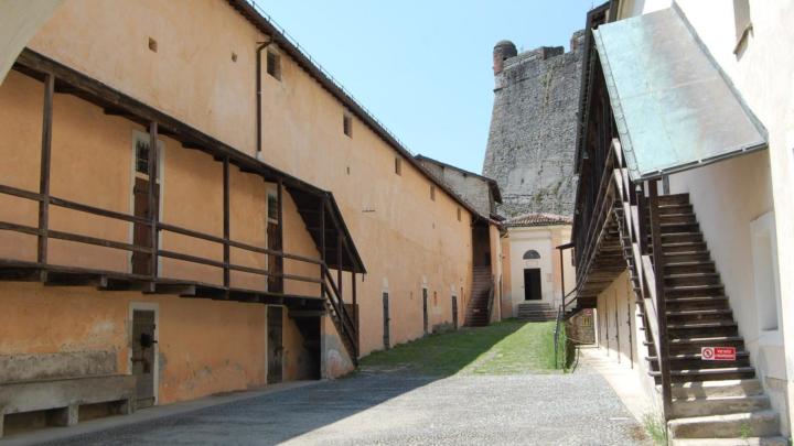 Coprtile inferno del Forte di Gavi con ballatoi in legno, scala esterna, sullo sfondo un alto bastione in pietra