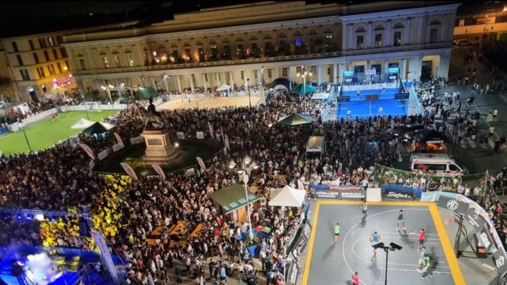 Piazza Martiri della Libertà a Novara in notturna: campetti sportivi e folla in una piazza porticata, intorno a monumento equestrentorno