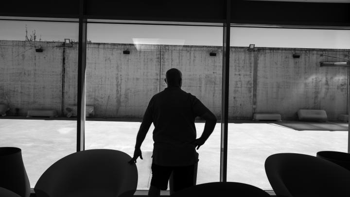 Particolare di foto di Daniele Robotti dal sito www.comune.alba.cn.it Un uomo in piedi e in controluce osserva un muro di recinzione di un carcere attraverso una vetrata